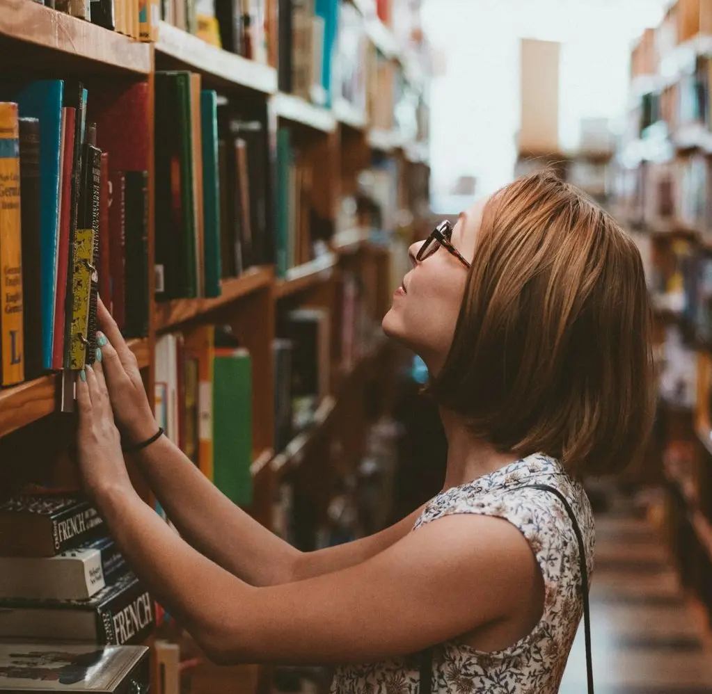 woman standing between library book shelves